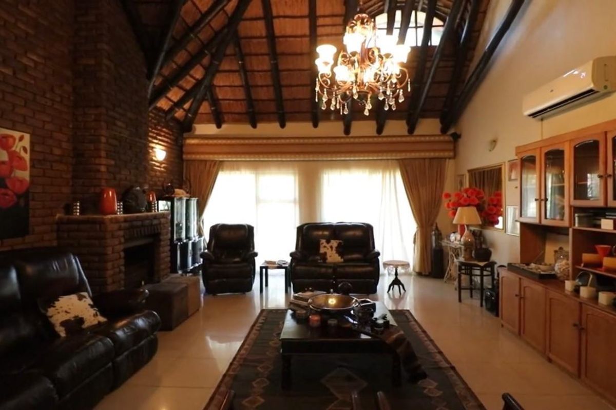 Spacious living room featuring a high vaulted thatched ceiling with exposed timber rafters, a prominent brick fireplace, and built-in wooden cabinetry.