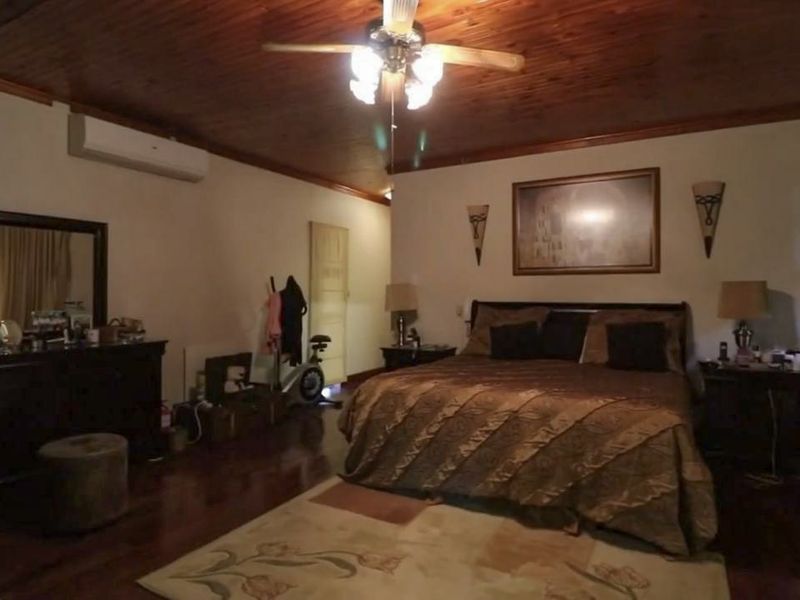 Spacious bedroom featuring a warm timber ceiling, hardwood flooring, and a wall-mounted split-system air conditioner for climate control.
