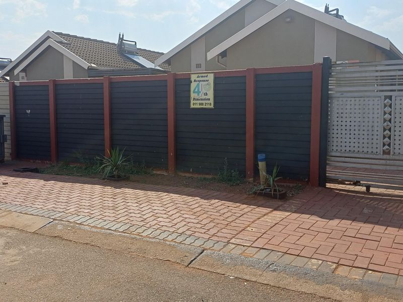 Front exterior view of the property featuring a dark horizontal slat perimeter fence, sliding gate, and paved driveway area.