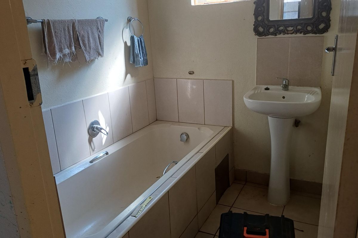 A functional bathroom featuring a pedestal basin and a built-in bathtub with tiled splashbacks, requiring cosmetic updates to improve its overall condition.