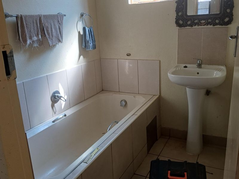 A functional bathroom featuring a pedestal basin and a built-in bathtub with tiled splashbacks, requiring cosmetic updates to improve its overall condition.