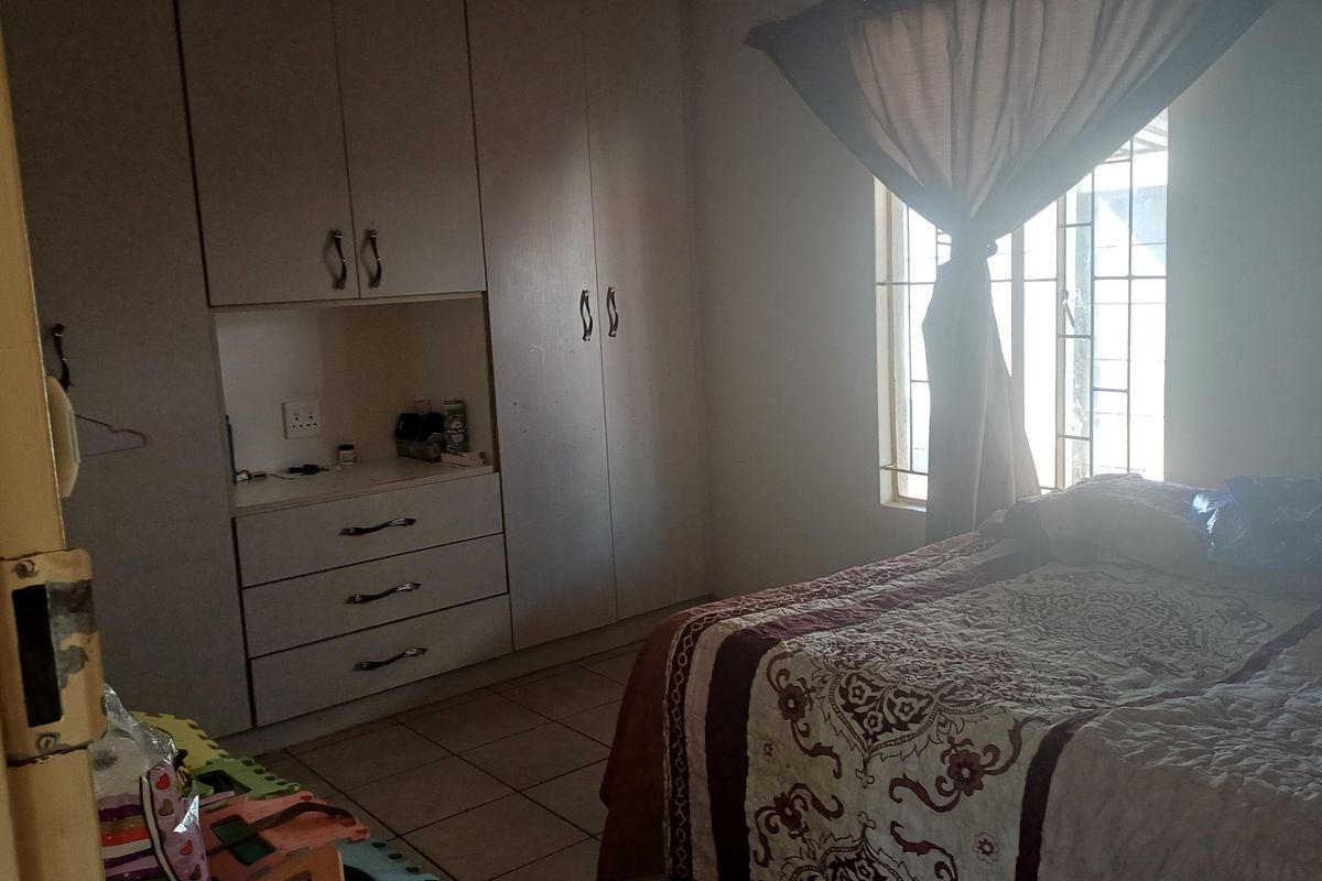 A bedroom featuring built-in cupboards, tiled flooring, and security bars on the window, offering a functional living space.