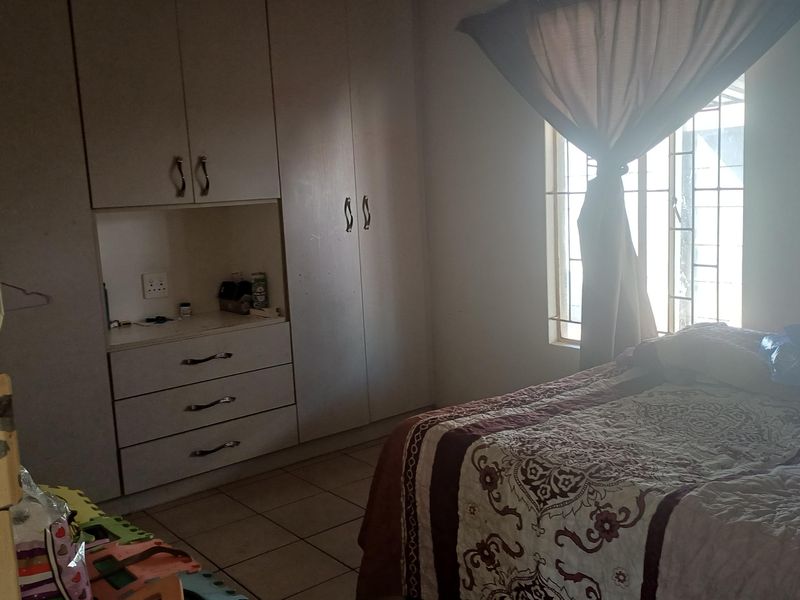 A bedroom featuring built-in cupboards, tiled flooring, and security bars on the window, offering a functional living space.