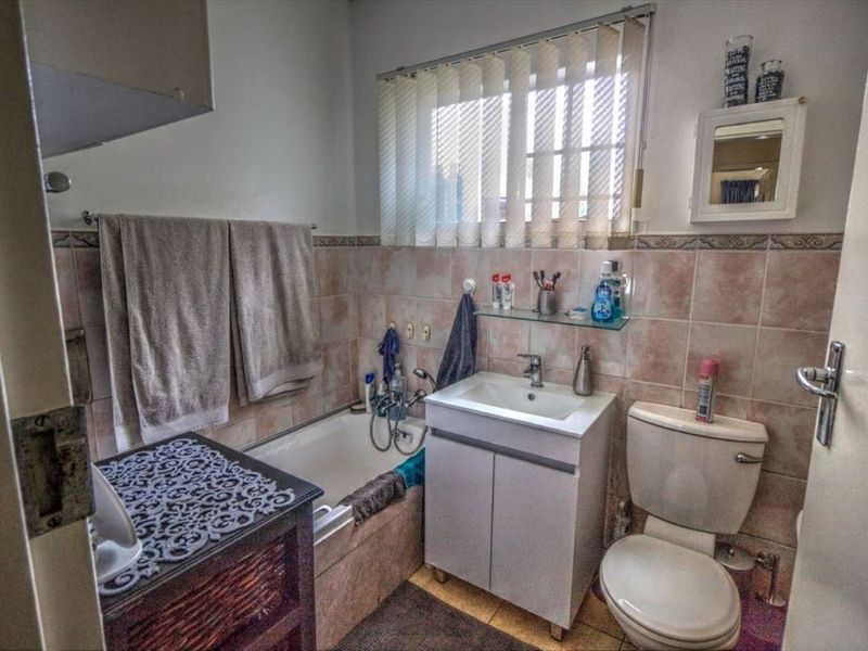 A functional bathroom featuring a bathtub, vanity cabinet with washbasin, toilet, and tiled finishes throughout.
