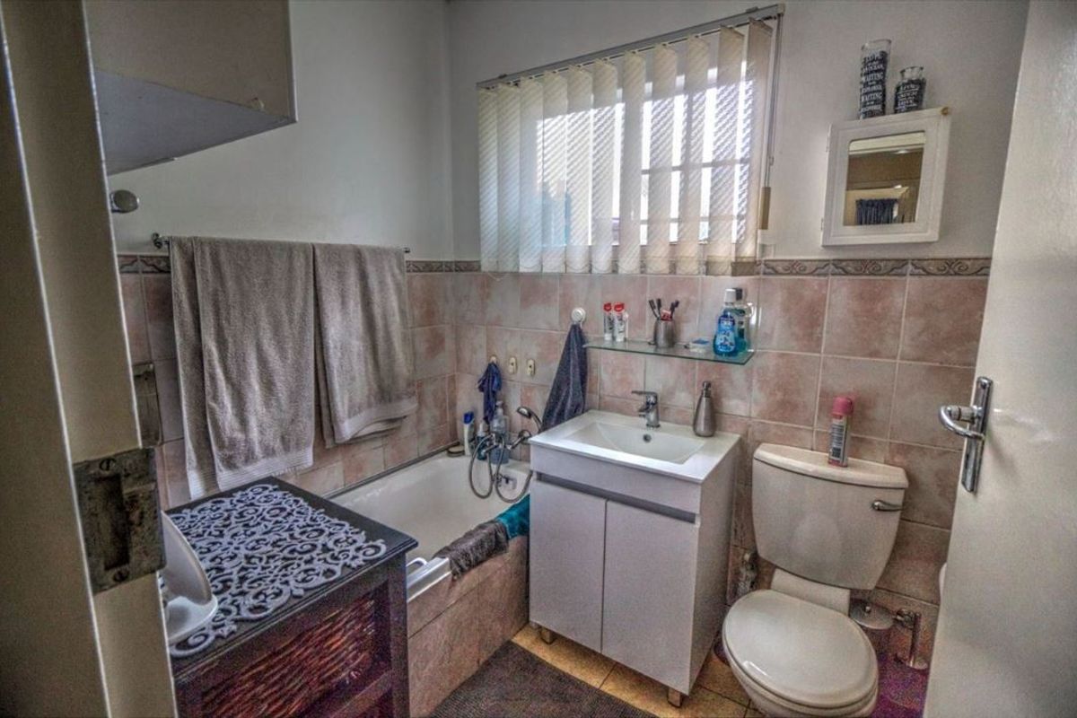 A functional bathroom featuring a bathtub, vanity cabinet with washbasin, toilet, and tiled finishes throughout.