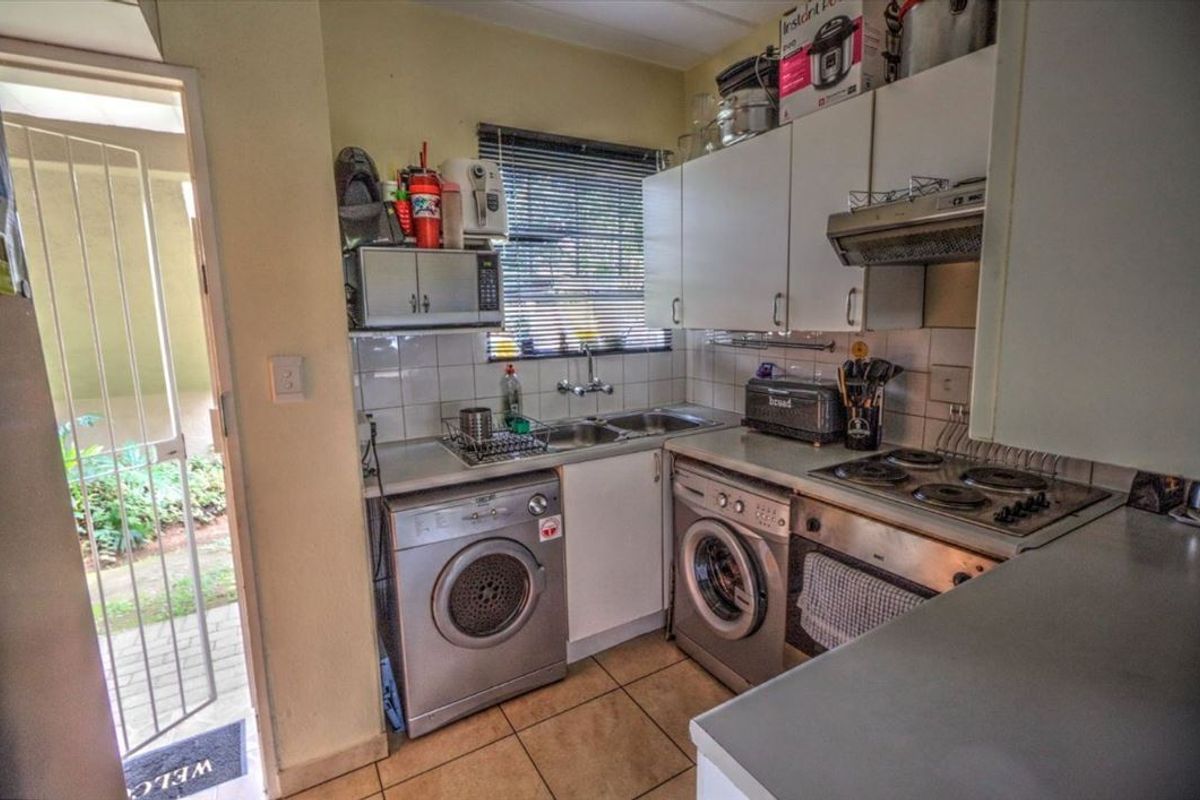 Compact kitchen featuring built-in cabinetry, electric stove with extractor, double sink, and direct access to an exterior area through a security gate.