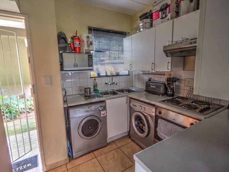 Compact kitchen featuring built-in cabinetry, electric stove with extractor, double sink, and direct access to an exterior area through a security gate.
