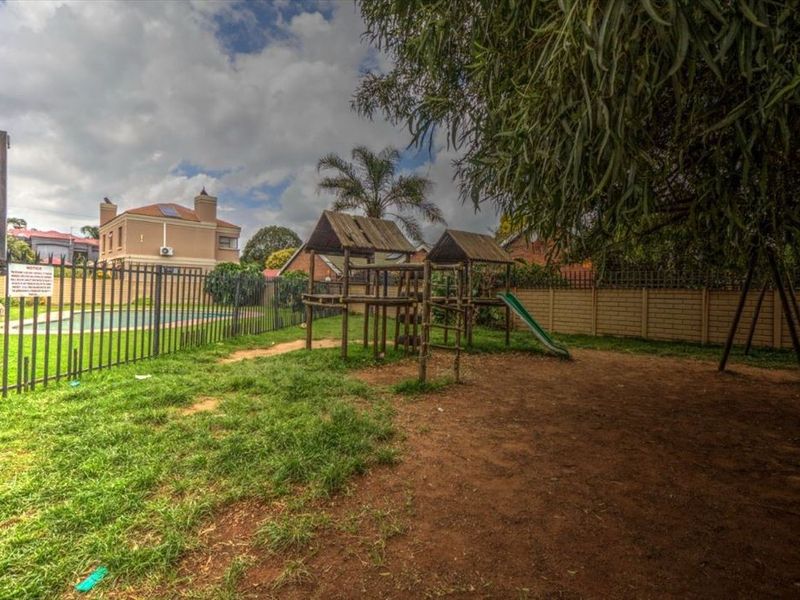A communal garden area featuring a swimming pool, metal perimeter fencing, and a brick boundary wall within a residential townhouse complex.