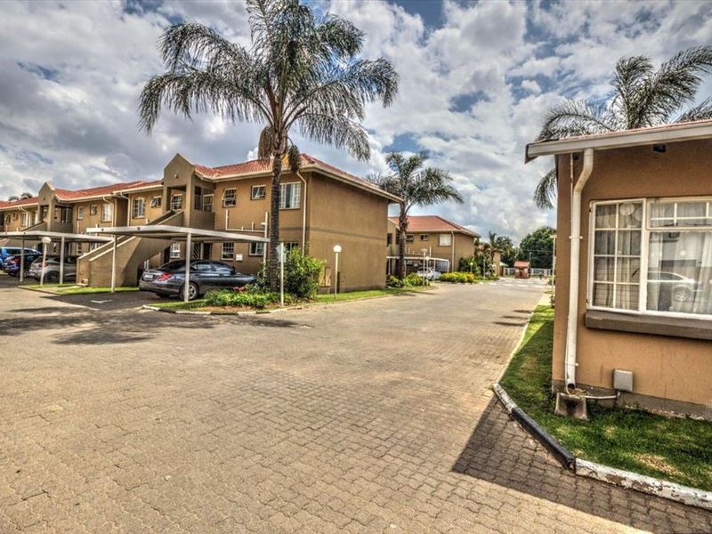 Exterior view of a townhouse complex featuring paved driveways, covered carports, and multi-story residential units with tiled roofs.