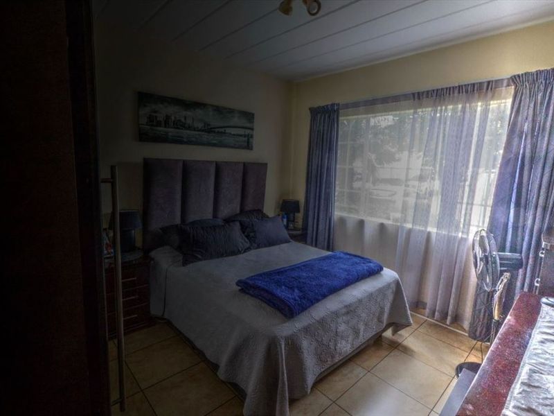 A bedroom featuring tiled flooring and large windows with curtain rails, providing natural light and a functional layout.
