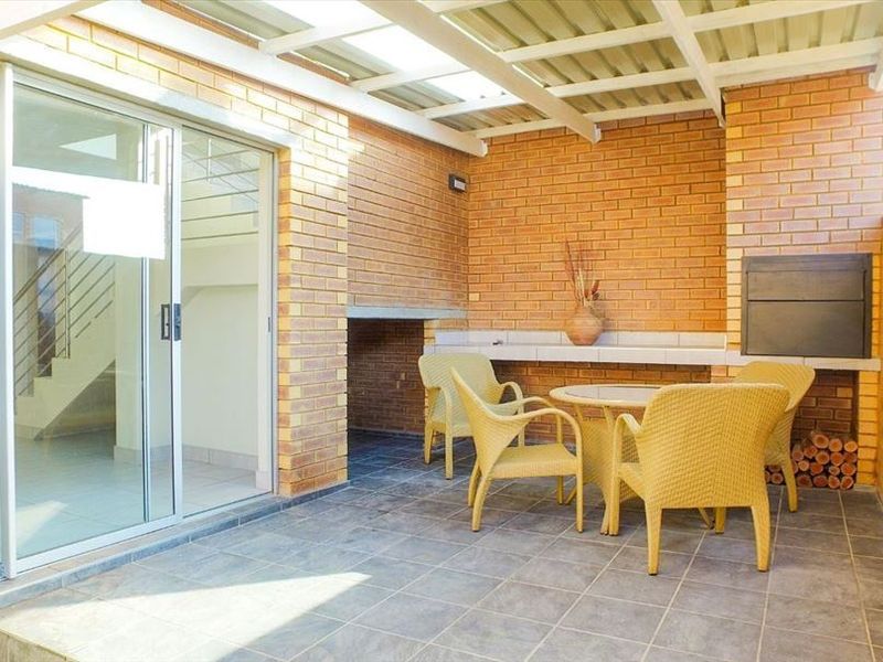 Covered patio area featuring exposed brick walls, tiled flooring, and a built-in braai, providing a functional outdoor entertainment space.