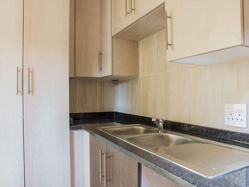 A clean and functional kitchen area featuring light wood-tone cabinetry, dark granite countertops, and a stainless steel double sink with tiled backsplash.