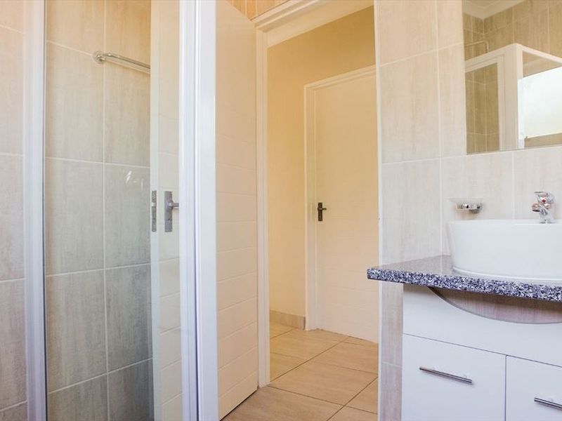A clean, functional bathroom featuring a shower enclosure, a modern vessel sink set on a granite countertop vanity, and neutral wall and floor tiling.