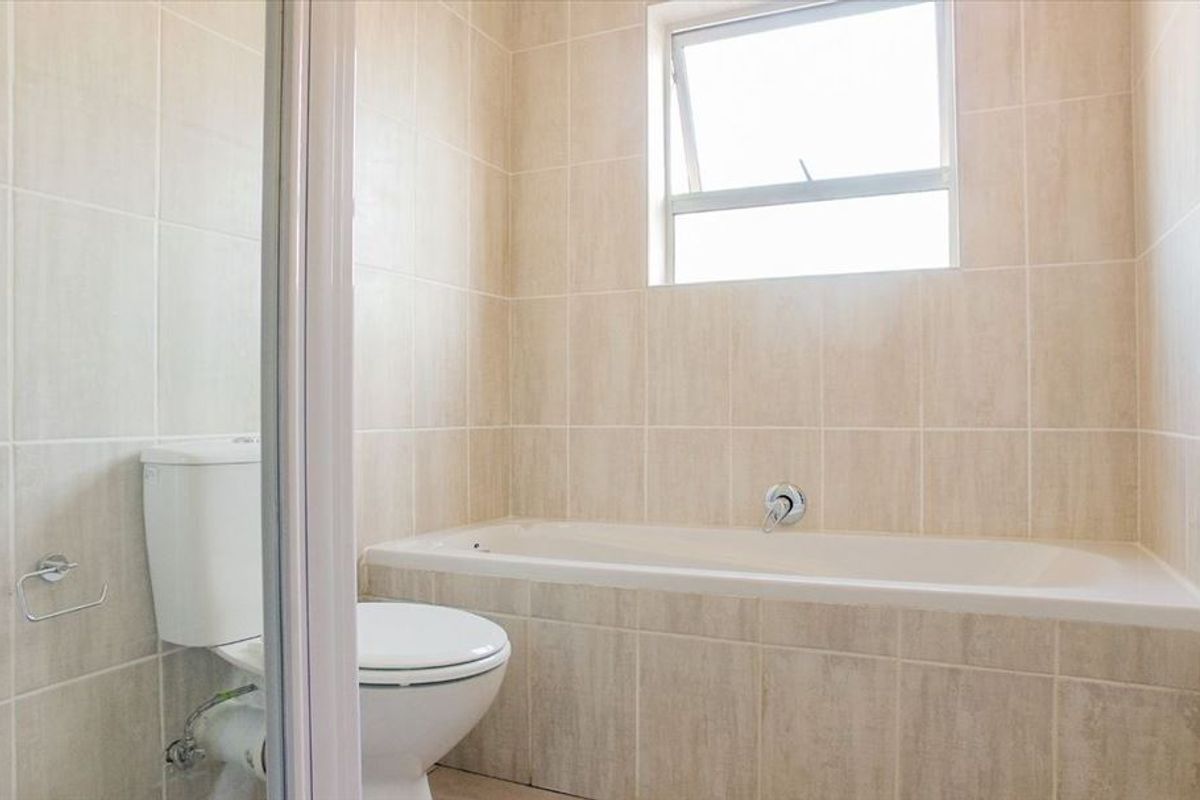 A clean, neutral-toned bathroom featuring a built-in bathtub, a separate shower enclosure, and a toilet, finished with floor-to-ceiling wall tiles.