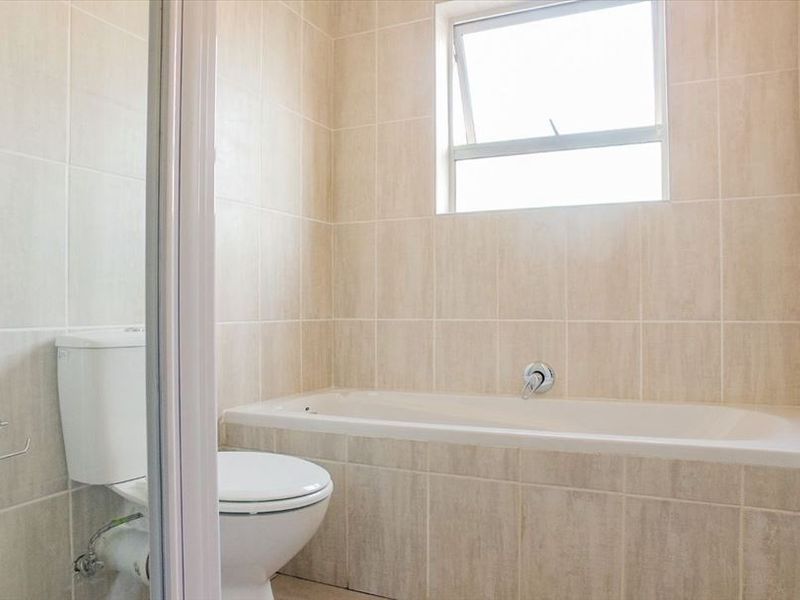 A clean, neutral-toned bathroom featuring a built-in bathtub, a separate shower enclosure, and a toilet, finished with floor-to-ceiling wall tiles.