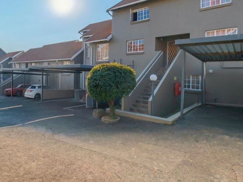 Exterior view of an apartment complex featuring covered parking carports, paved driveway, and external staircase access to upper units.