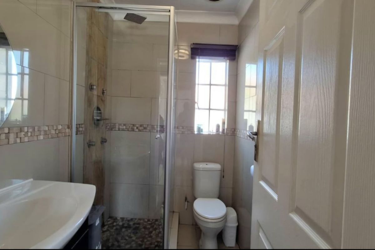 A functional bathroom featuring a glass-enclosed shower with pebble flooring, a vanity basin, and neutral wall tiling.