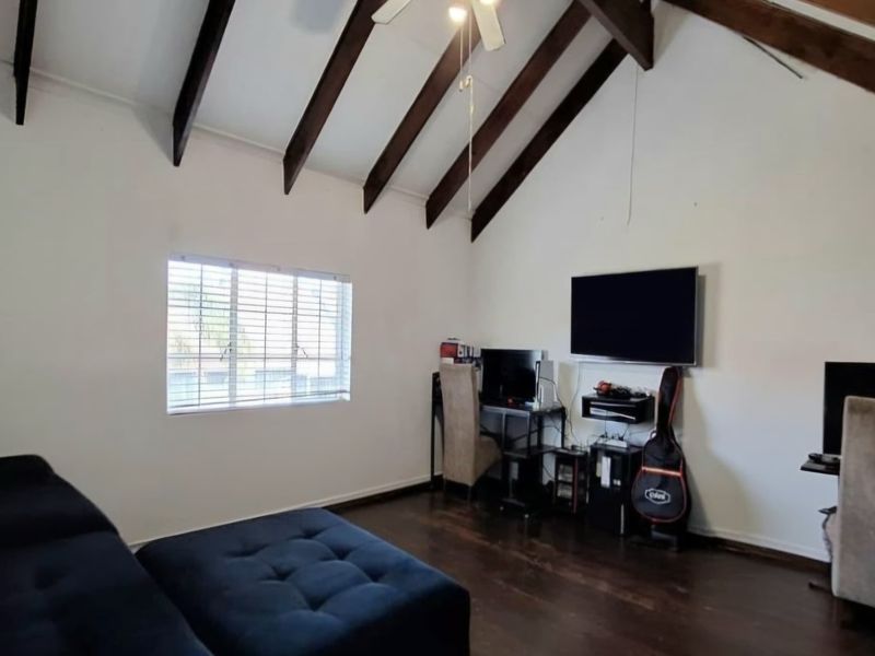 Spacious living room featuring high vaulted ceilings with exposed timber beams, dark timber flooring, and natural light through venetian blinds.