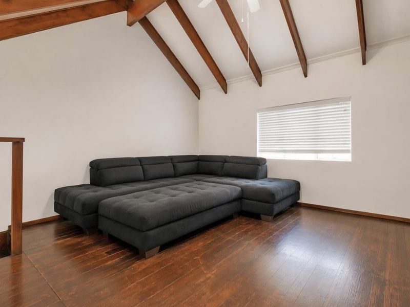 Spacious living area featuring high vaulted ceilings with exposed timber beams, dark timber flooring, and a staircase with a wooden balustrade.