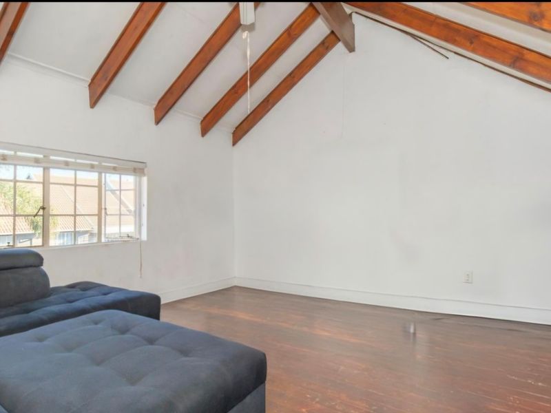 Spacious living area featuring a vaulted ceiling with exposed timber beams, timber flooring, and natural light from a casement window.
