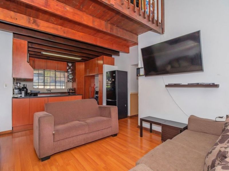 Open-plan living area featuring exposed timber ceiling beams, a mezzanine level, and a functional kitchen with wood-finish cabinetry and laminate flooring.