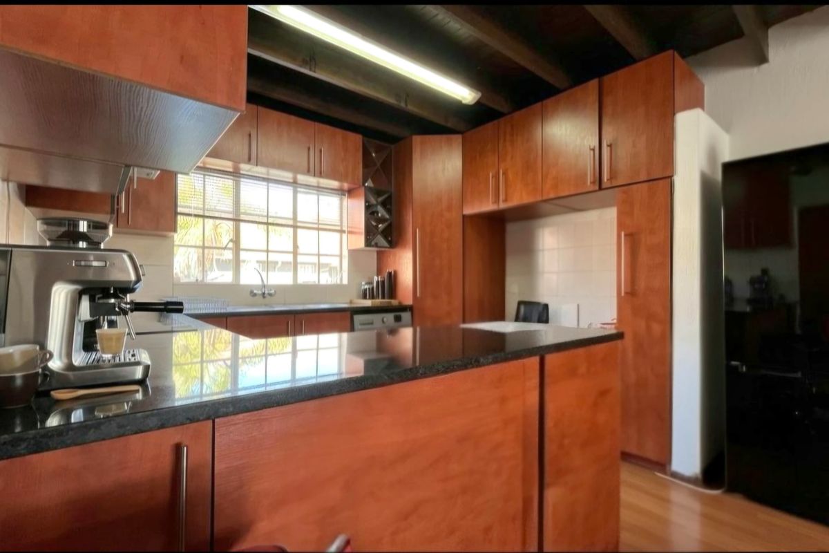 A functional kitchen featuring warm-toned laminate cabinetry, granite countertops, and exposed timber ceiling beams, offering a classic aesthetic with ample storage space.