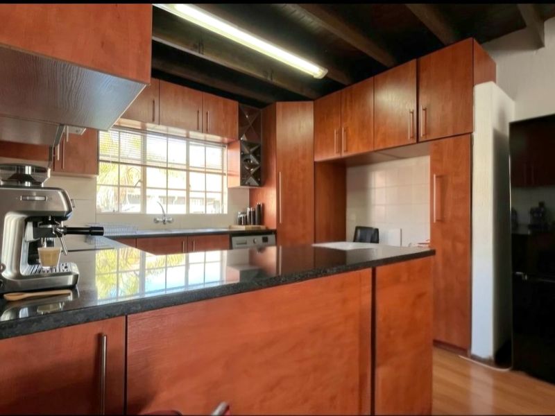 A functional kitchen featuring warm-toned laminate cabinetry, granite countertops, and exposed timber ceiling beams, offering a classic aesthetic with ample storage space.