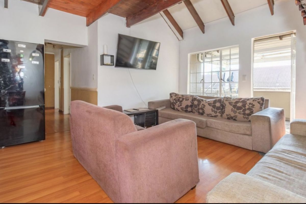 Living room featuring exposed timber ceiling beams, laminate flooring, and access to an outdoor balcony area.