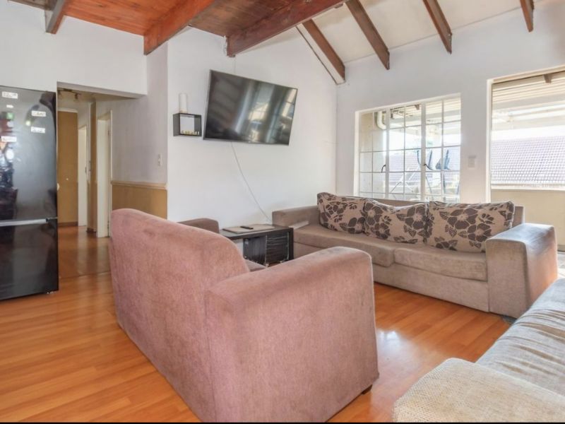 Living room featuring exposed timber ceiling beams, laminate flooring, and access to an outdoor balcony area.