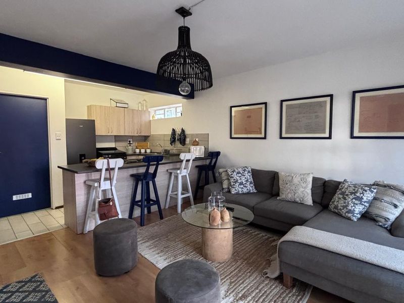 An open-plan living and kitchen area featuring laminate flooring, modern cabinetry, and a breakfast bar, creating a functional and cohesive living space.