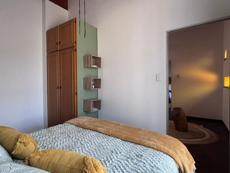A bedroom featuring a built-in wooden wardrobe and wall-mounted shelving, with a doorway leading to an adjacent room.
