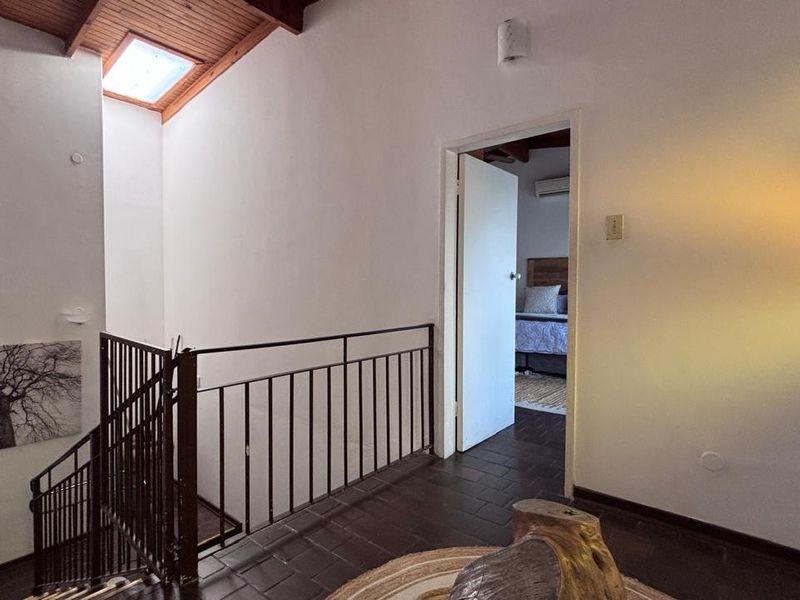 A bright hallway featuring a timber-lined ceiling with a skylight, dark tiled flooring, and a metal balustrade overlooking the staircase.