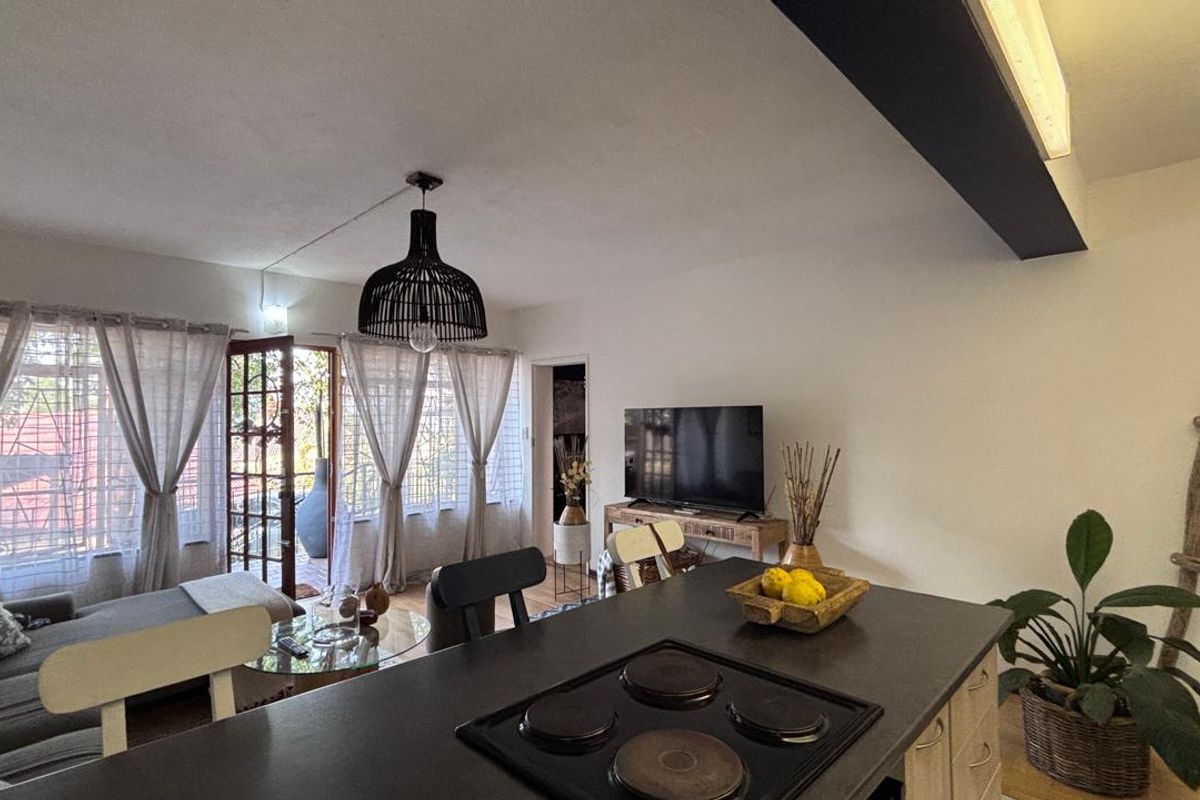 Open plan living area featuring a kitchen island with an integrated electric hob, flowing into a lounge space with direct access to an outdoor area.