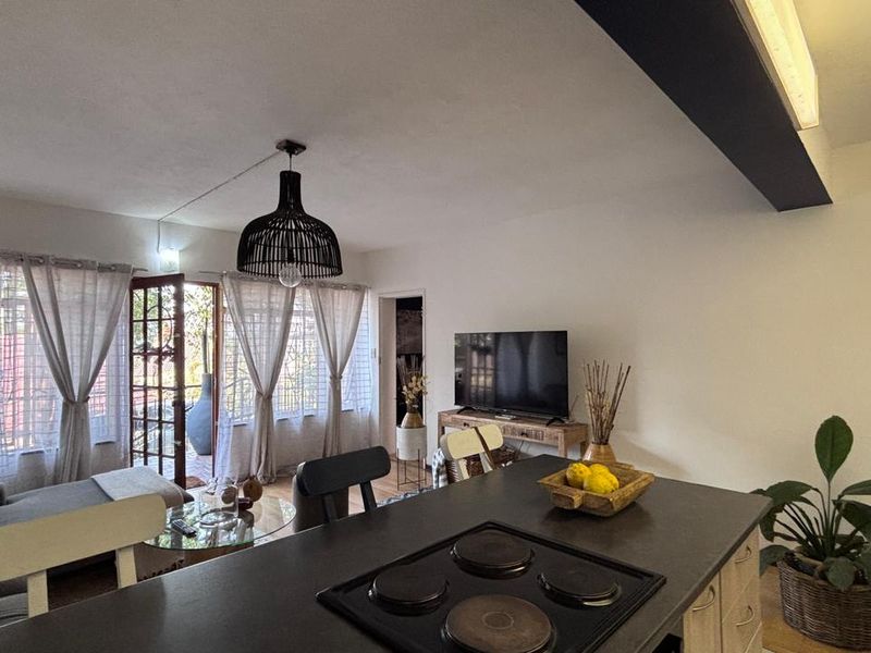 Open plan living area featuring a kitchen island with an integrated electric hob, flowing into a lounge space with direct access to an outdoor area.