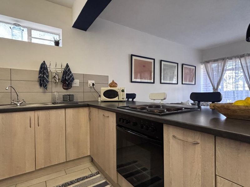 Open-plan kitchen featuring light wood-finish cabinetry, dark laminate countertops, built-in oven and hob, and tiled backsplash, seamlessly flowing into the living area.