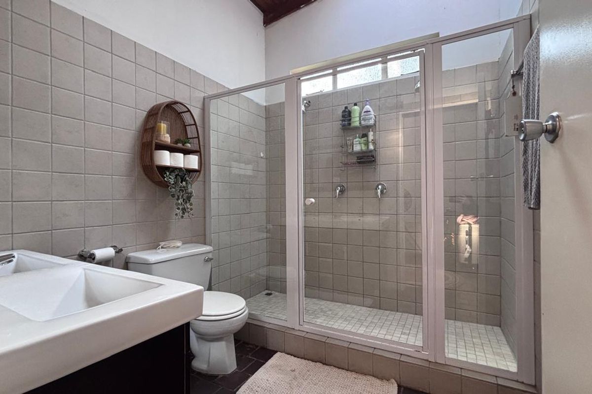 A functional bathroom featuring a walk-in shower with a glass enclosure, neutral ceramic wall tiling, a vanity basin, and a standard toilet.
