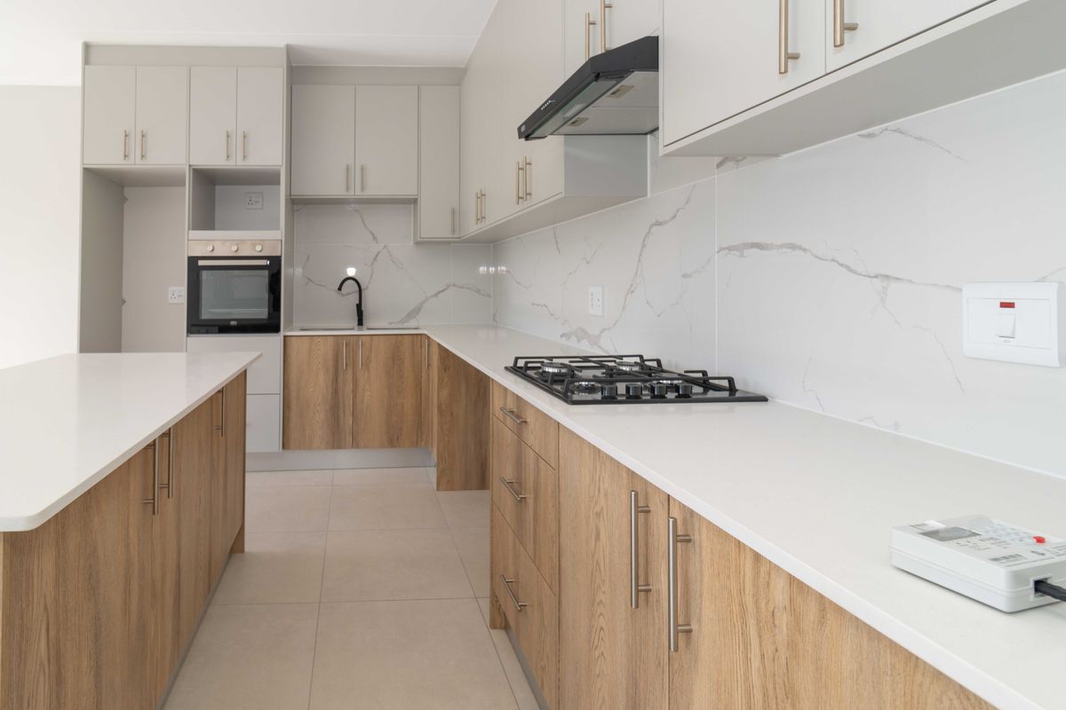 Modern kitchen featuring light wood-grain cabinetry, white stone countertops, marble-look splashback, built-in oven, gas hob, and a functional kitchen island.