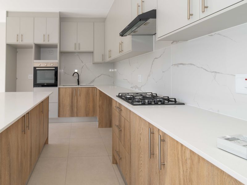 Modern kitchen featuring light wood-grain cabinetry, white stone countertops, marble-look splashback, built-in oven, gas hob, and a functional kitchen island.