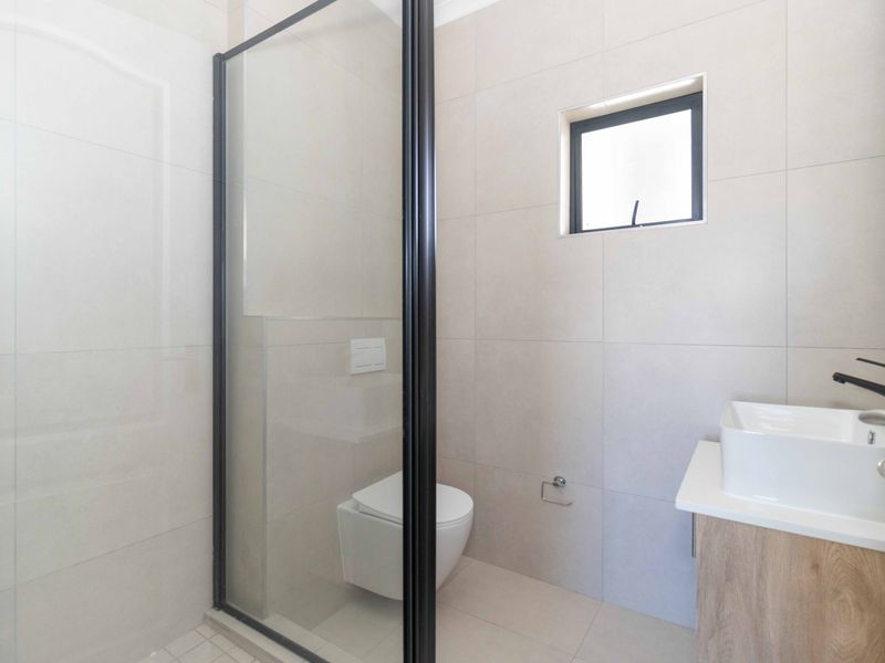 Modern bathroom featuring a wall-hung toilet, glass shower enclosure with black framing, and a contemporary vessel sink vanity.