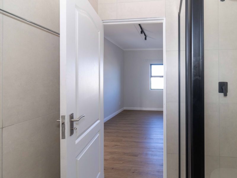 A view from a tiled bathroom looking through a doorway into an empty bedroom with wood-look flooring and neutral walls.