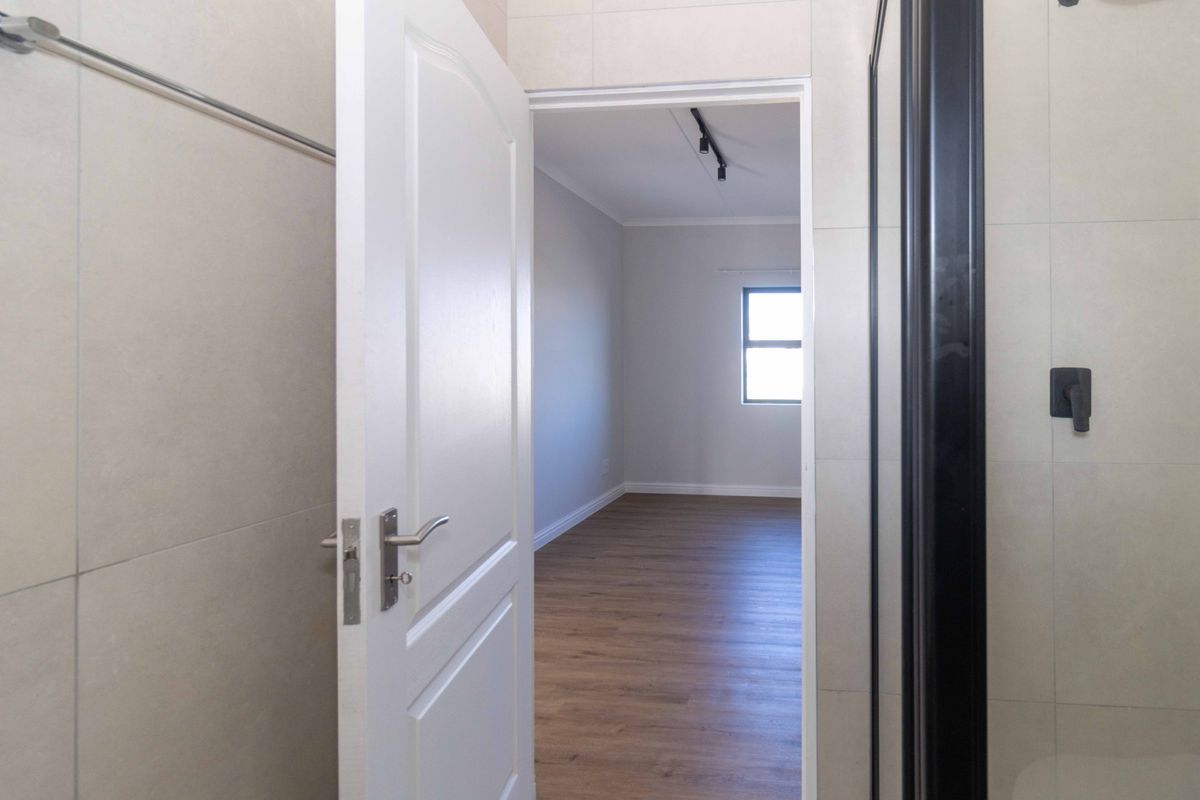 A view from a tiled bathroom looking through a doorway into an empty bedroom with wood-look flooring and neutral walls.