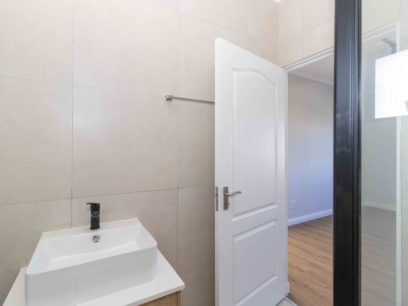 A modern bathroom featuring a sleek vessel sink with a black faucet, neutral wall tiling, and a glass shower partition.