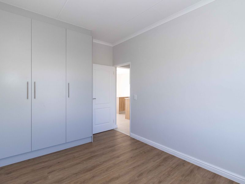 A bright, empty bedroom featuring modern light-toned built-in cupboards and wood-look laminate flooring, offering a clean and neutral space ready for personalization.