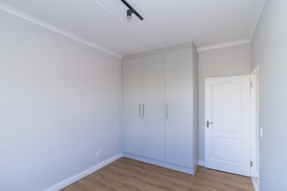 A clean, neutral bedroom featuring modern laminate flooring, built-in wardrobe storage, and contemporary track lighting.