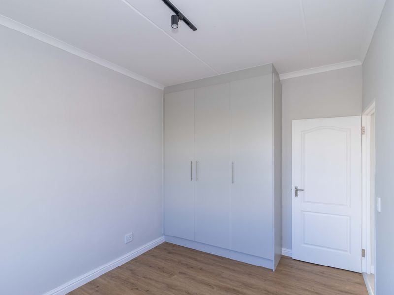 A clean, neutral bedroom featuring modern laminate flooring, built-in wardrobe storage, and contemporary track lighting.
