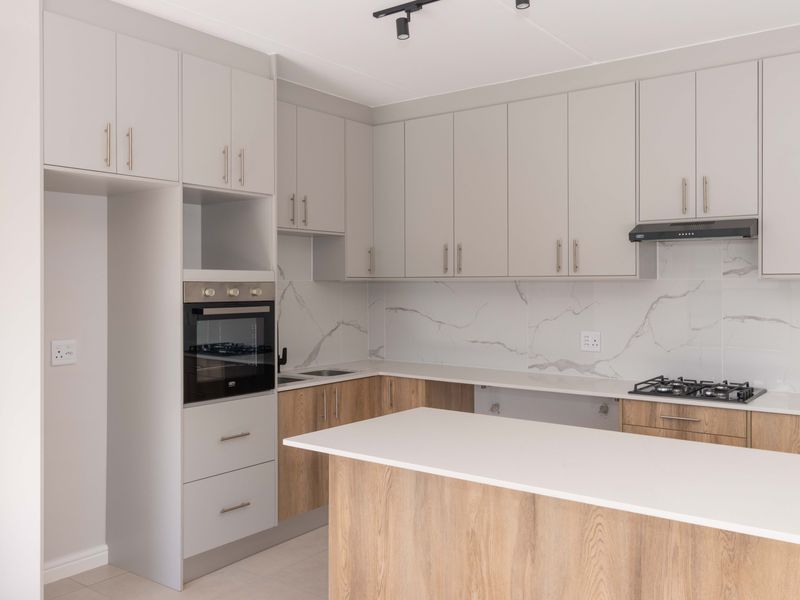 Modern kitchen featuring two-tone cabinetry, quartz countertops, marble-look splashback, built-in oven, gas hob, and a functional kitchen island.