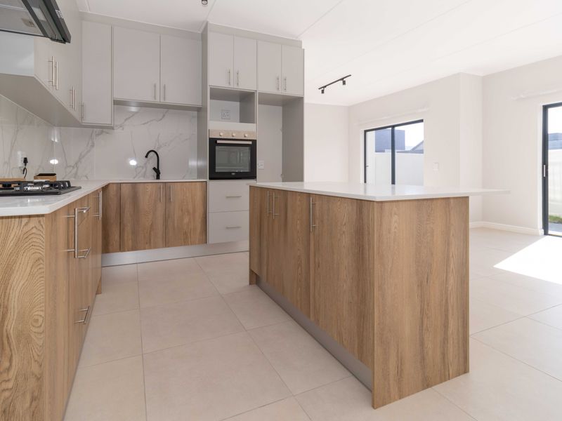 Modern open-plan kitchen featuring wood-finish cabinetry, stone countertops, built-in appliances, and a central island, flowing into a bright living area with sliding door access.