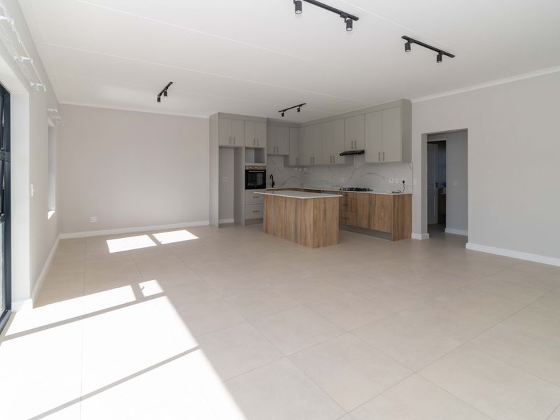 Spacious open-plan living and kitchen area featuring modern cabinetry, stone countertops, built-in appliances, tiled flooring, and large sliding doors leading to the exterior.