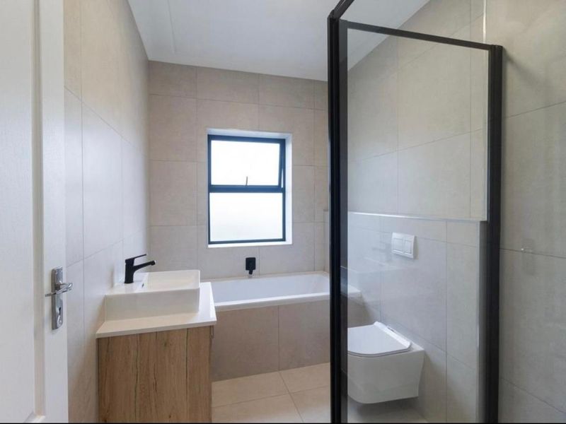 Modern bathroom featuring a built-in vanity, bathtub, wall-mounted toilet, and a glass-enclosed shower with contemporary black fixtures and neutral tiling.