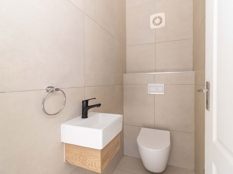A modern, compact guest bathroom featuring neutral wall tiles, a wall-mounted vanity basin with a black tap, and a wall-hung toilet.